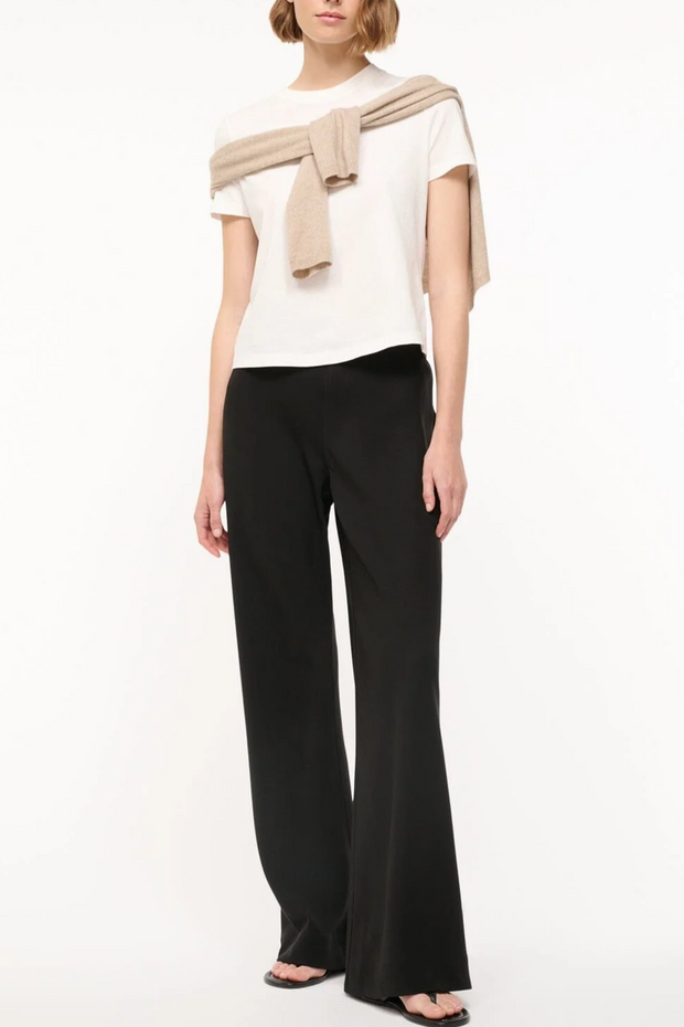 Woman wearing a white top, black pants, and a beige sweater on a white background