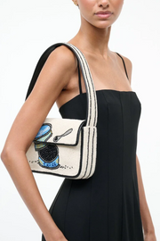 Woman wearing a black dress with a white crossbody bag featuring a design of a teacup and spoon.