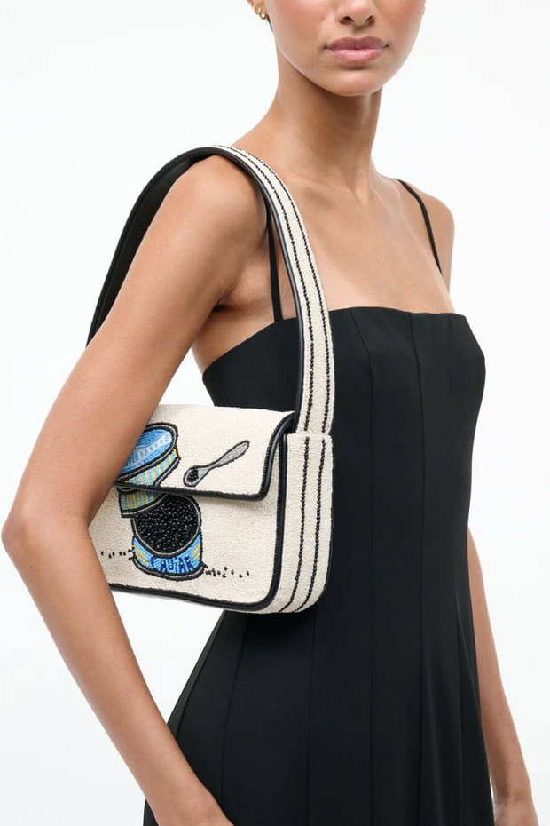 Woman wearing a black dress with a white crossbody bag featuring a design of a teacup and spoon.