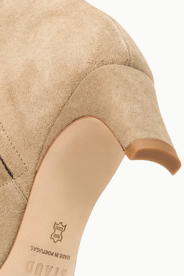 Close-up of a beige suede shoe with a brand logo on a white background
