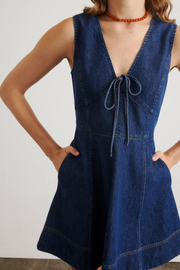 Person wearing a blue denim dress with a plain background