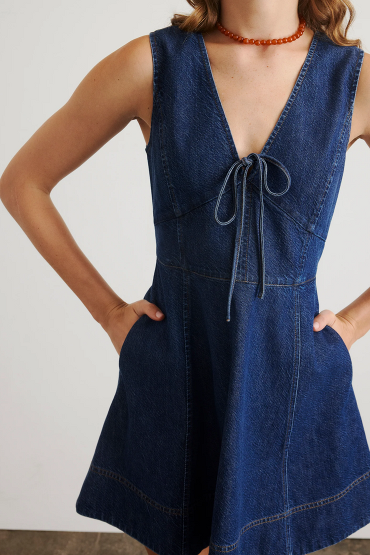 Person wearing a blue denim dress with a plain background