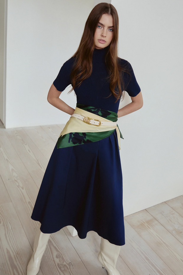 Woman wearing a navy dress with a floral belt in a minimal indoor setting