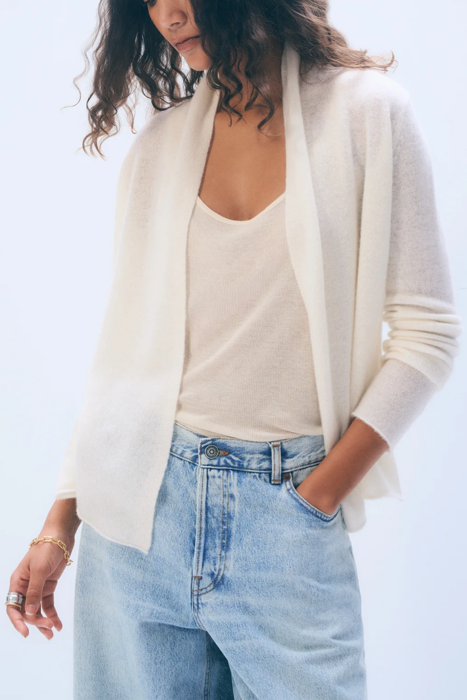 Person wearing a white cardigan, white top, and light blue jeans against a light background