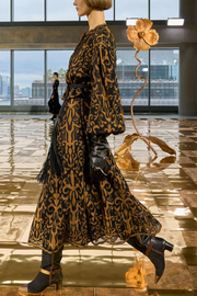 Woman in a printed jacket and skirt standing in a modern indoor setting with large windows.