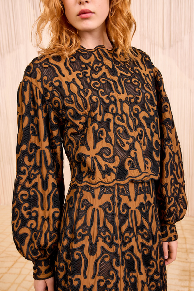 Person wearing a brown and black patterned jacket against a light wooden background