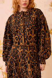 Person wearing a black and brown patterned jacket and skirt  against a beige background