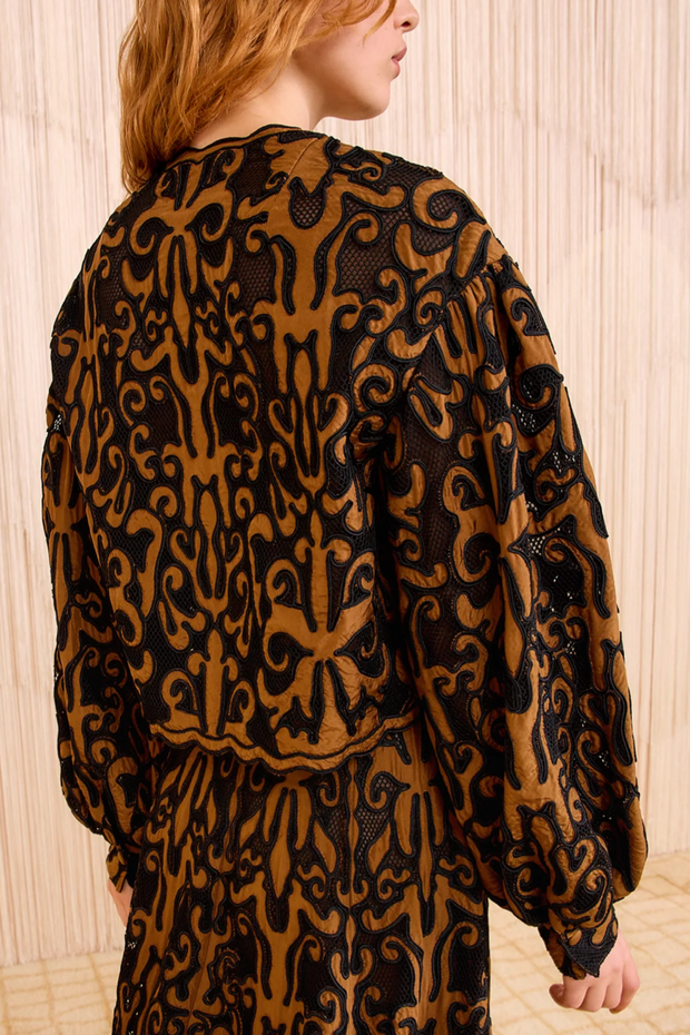 Person wearing a black and brown patterned jacket and skirt against a neutral background