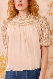 Woman wearing a beige blouse with lace details on a floral background