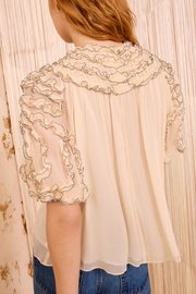 Light beige blouse with floral lace details worn by a person, against a neutral background.