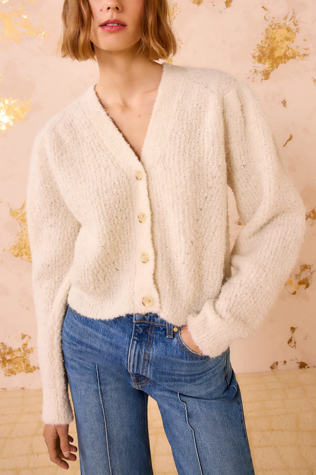 Person wearing a cardigan and blue jeans against a decorative wall.