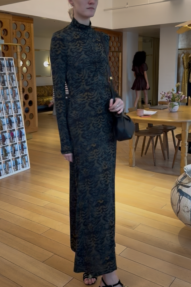 Person wearing a long dark green patterned dress in an indoor setting.
