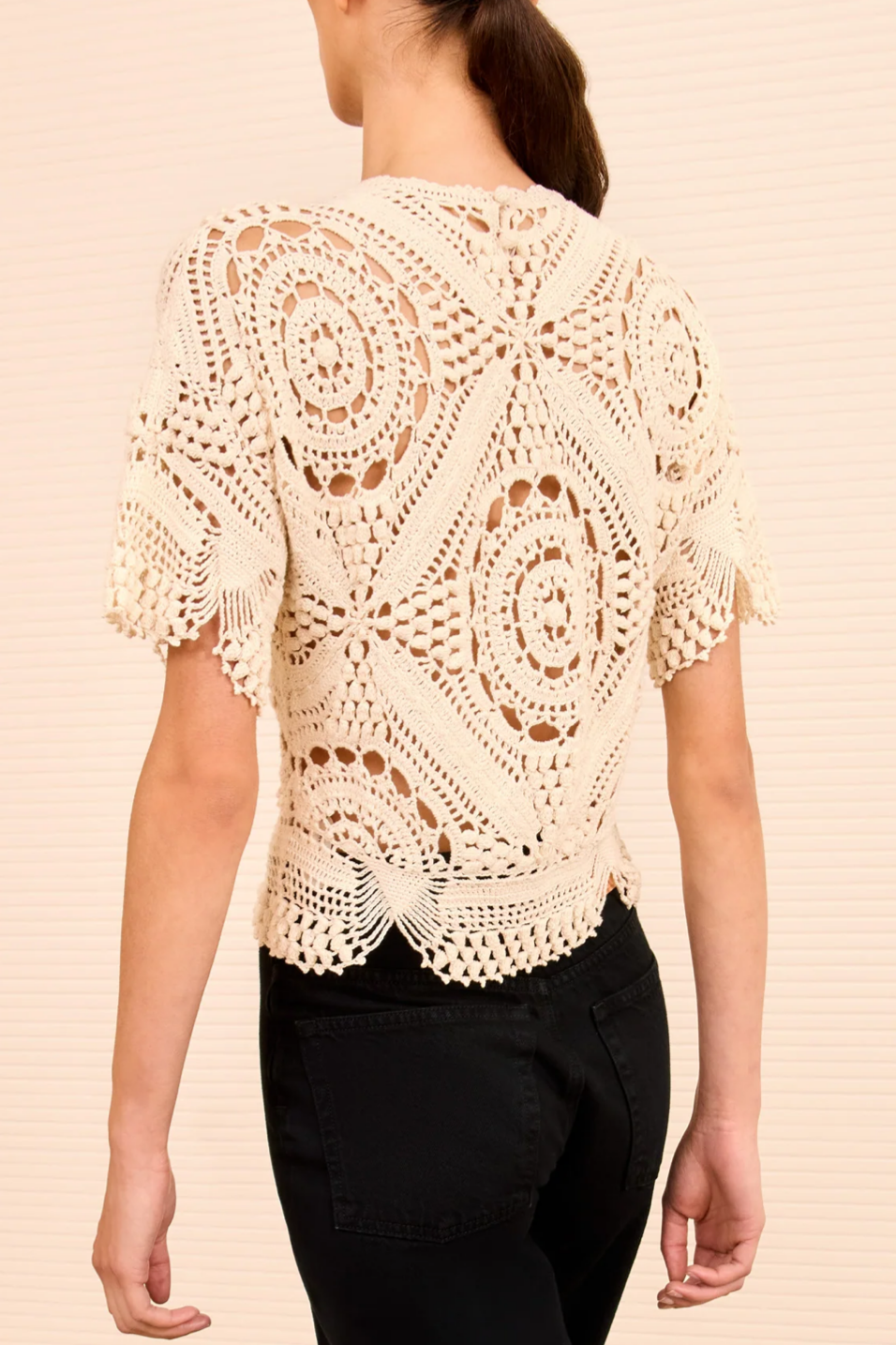 Woman wearing a beige crochet top against a beige background