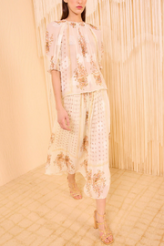 Woman wearing a cream-colored embroidered outfit with a textured beige wall background