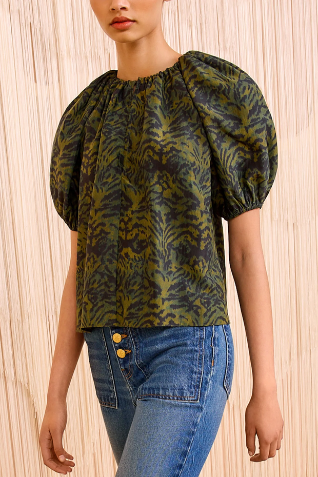 Woman wearing a green patterned blouse with puff sleeves and blue jeans on a beige background