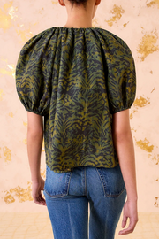 Person wearing a green pattern blouse with puffed sleeves against a beige background
