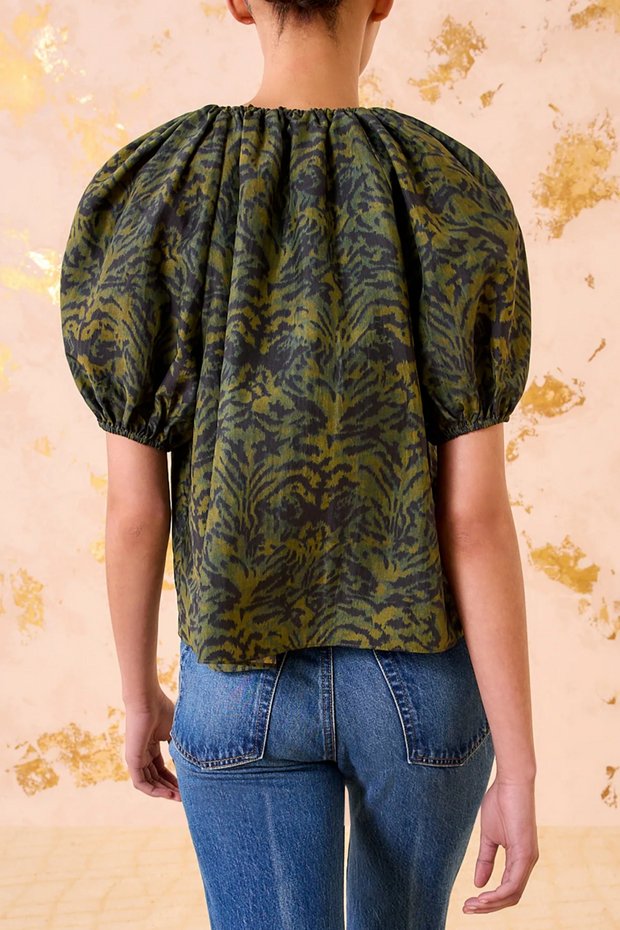 Person wearing a green pattern blouse with puffed sleeves against a beige background