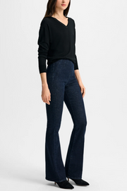 Woman wearing a black top and dark blue flared pants on a white background