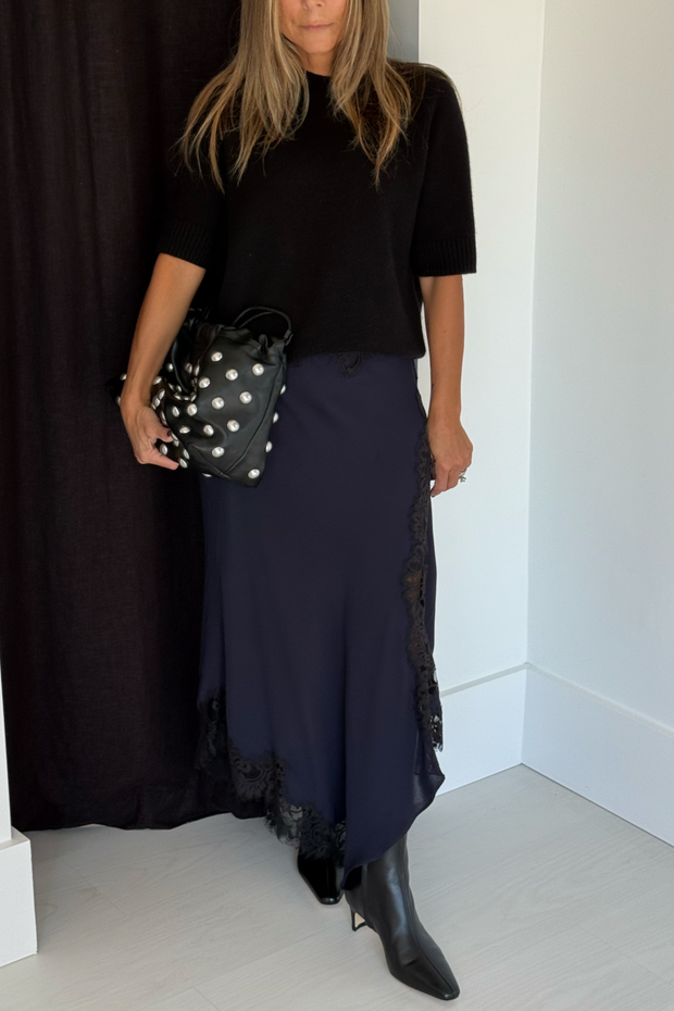 Person wearing a black top and navy skirt with lace details, holding a studded bag.