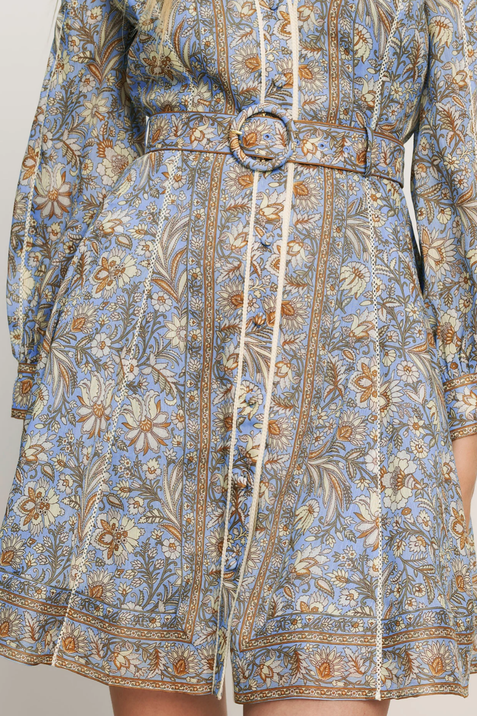 Close-up of a floral patterned dress with a belt on a plain background
