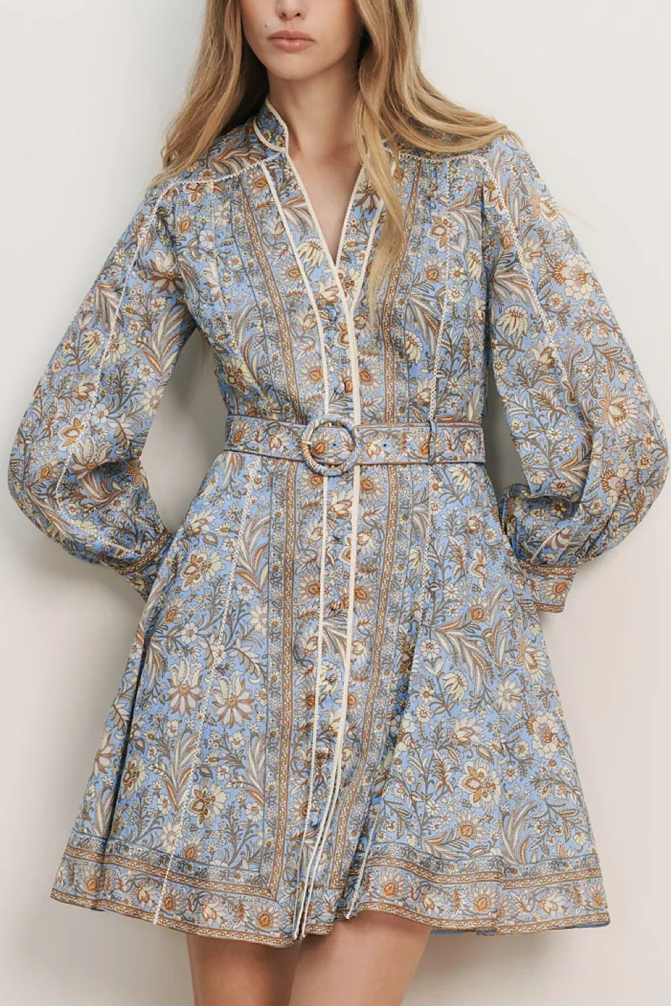 Woman wearing a floral patterned dress with a belt against a plain background