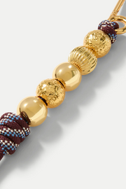 Bag charm with gold beads and maroon checkered pattern on a light gray background