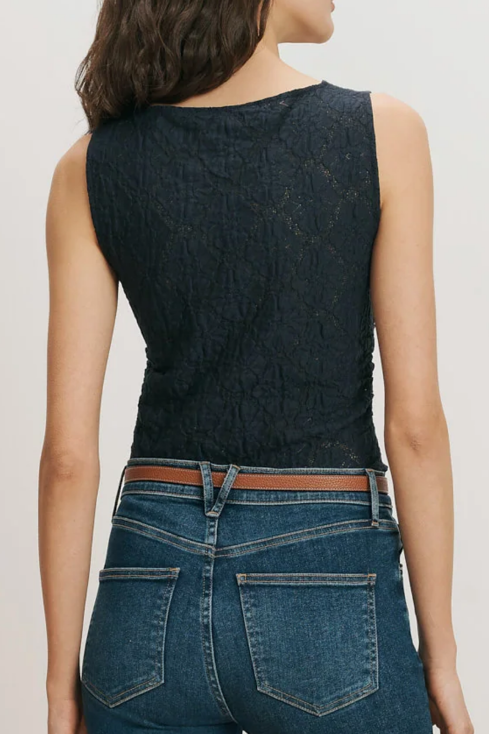 Person wearing a navy sleeveless top and blue jeans on a plain background