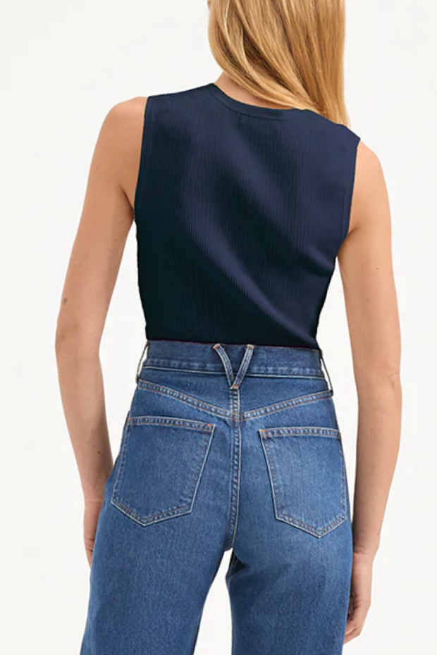 Person wearing a navy sleeveless top and blue jeans on a white background