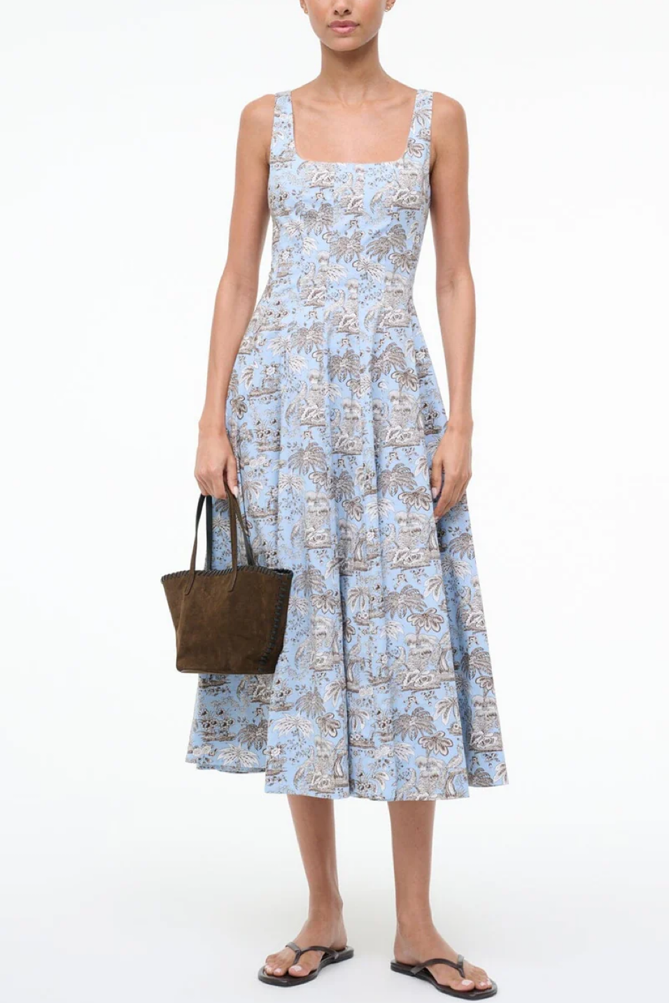 Woman wearing a light blue floral dress holding a brown bag on a white background